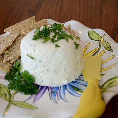 Mounded homemade boursin with parsley garnish on a serving plate with a dip spreader.