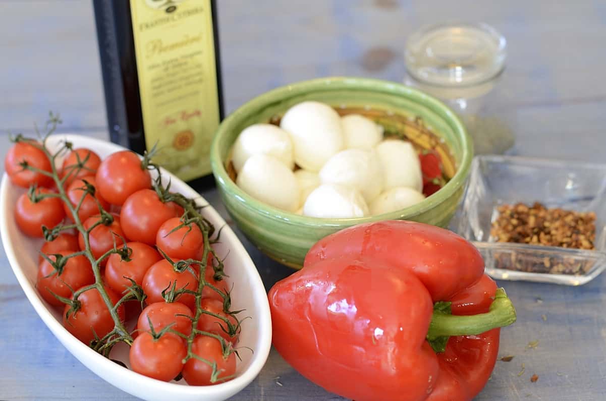 Cherry tomatoes, red pepper, bocconcini and olive oil on a table.