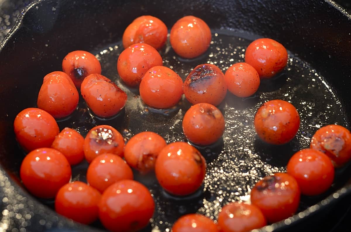 Charred cherry tomatoes in a cast iron skillet.