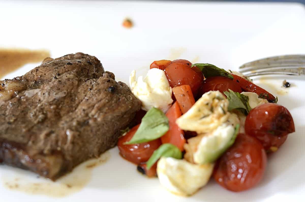 Juicy steak on a plate with a side of charred cherry tomato salad.