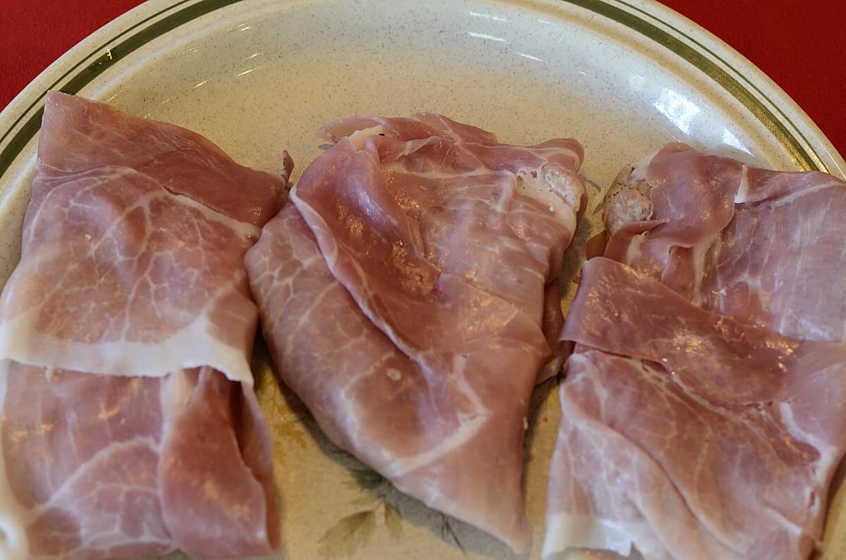 Pork scaloppini wrapped in prosciutto on a platter.