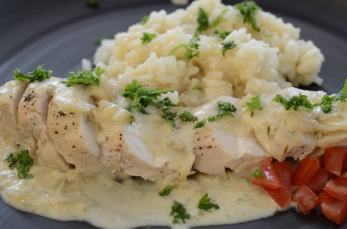 Sliced chicken on a plate with Champagne Sauce and Champagne Risotto on the side.