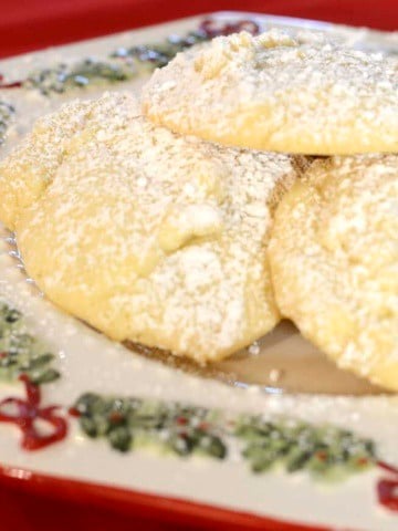 Fluffy white chocolate chip snowball cookies dusted with icing sugar on a Christmas plate.