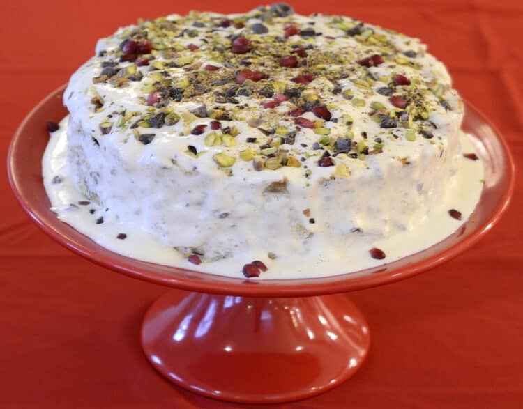 Italian Christmas Pudding Cake sprinkled with pistachios, chocolate chips and pomegranates seeds on a red pedestal plate.