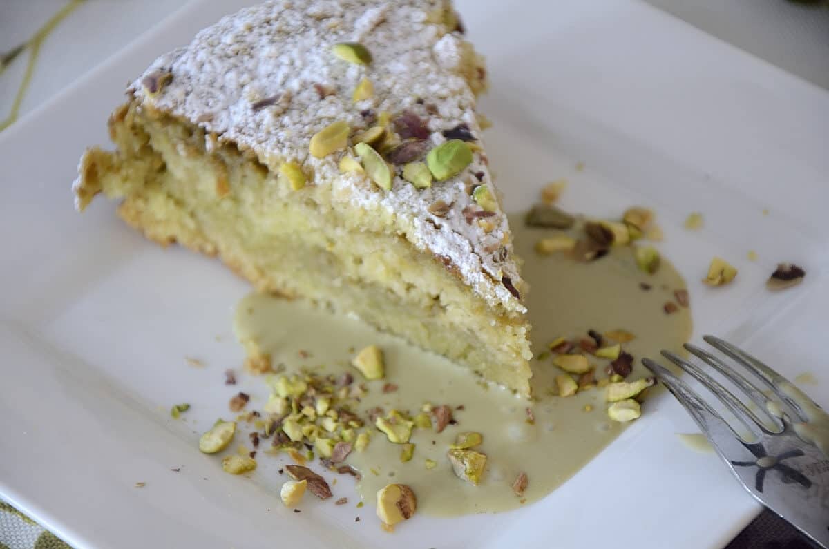 Piece of Italian crumb cake with pistachio cream filling, topped with crushed pistachios and icing sugar.