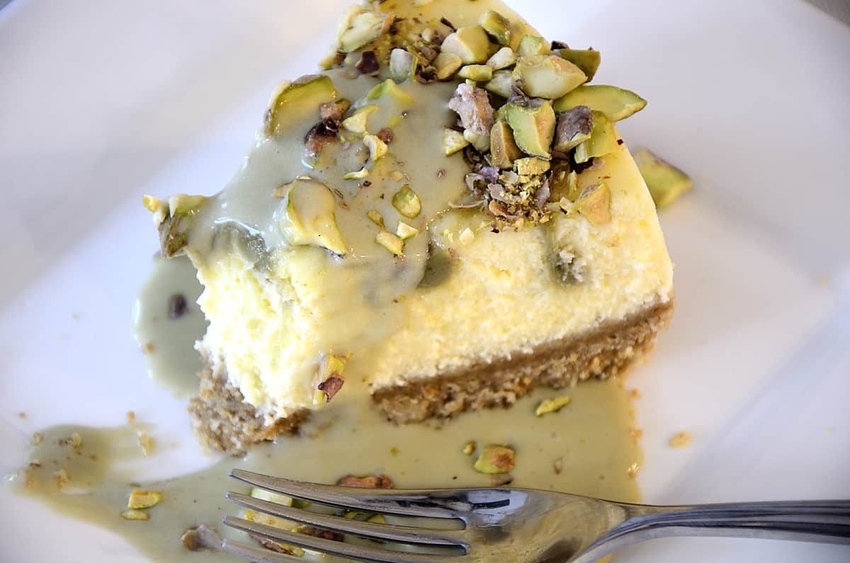Slice of pistachio cheesecake drizzle with pistachio cream and crushed nuts.