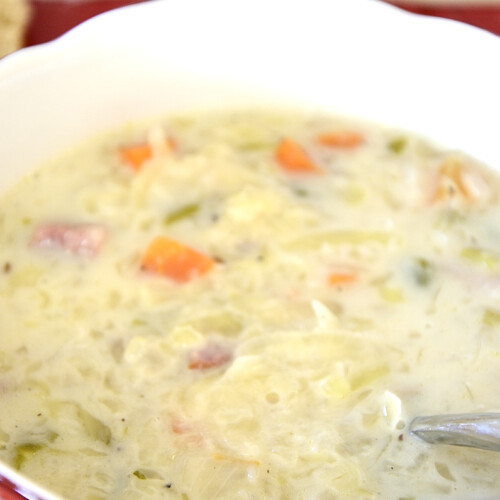Close up of a bowl of creamy cabbage soup with carrots, celery and sausage.