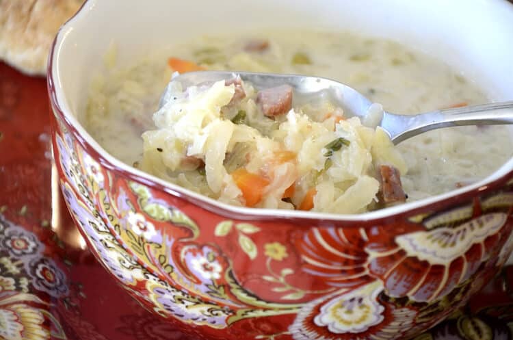 Close up of a bowl of creamy cabbage soup with carrots, celery and sausage.