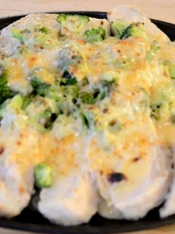 Platter of sliced chicken breast with a mound of broccoli covered in creamy sauce and cheese topping is broiled to golden brown.
