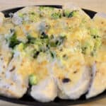 Platter of sliced chicken breast with a mound of broccoli covered in creamy sauce and cheese topping is broiled to golden brown.