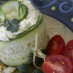 Cucumber collar filled with layers of salad, topped with egg salad and garnished with mustard caviar, grape tomatoes and cilantro.