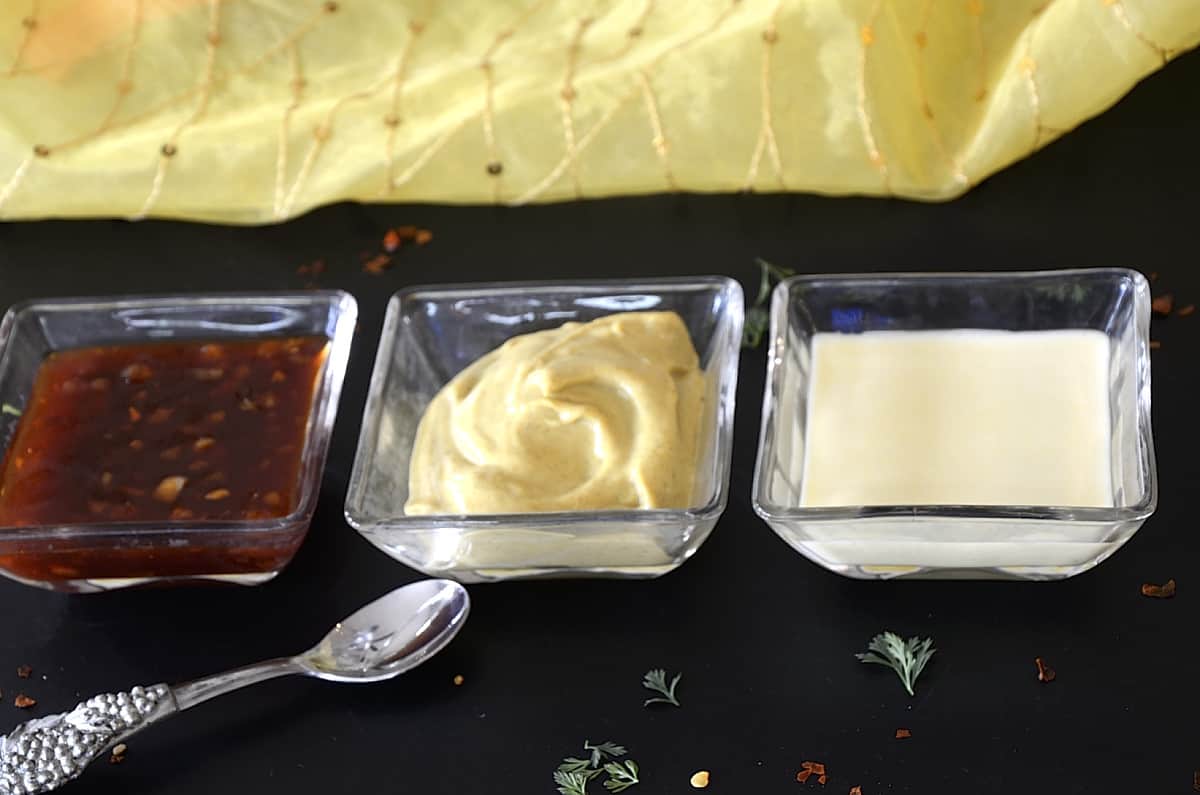 Trio of sauces including General Tso, Curry Mustard Mayonnaise and Champagne Aioli in small dishes.