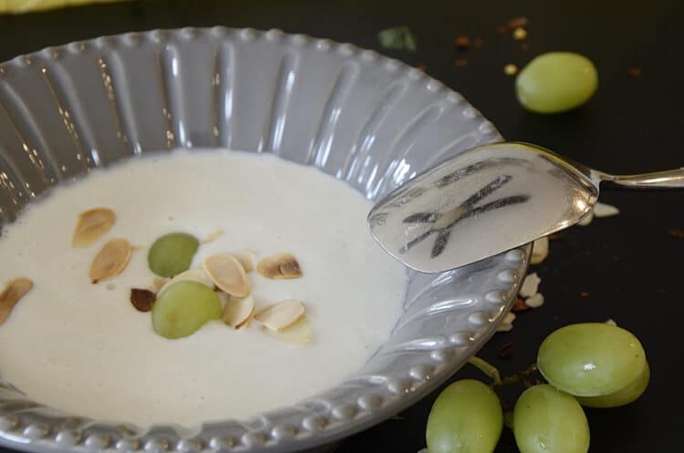 A bowl of cold, creamy, almond soup with toasted almond and green grape garnish.