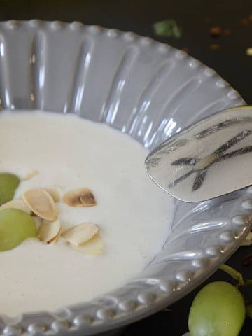 A bowl of cold, creamy, almond soup with toasted almond and green grape garnish.