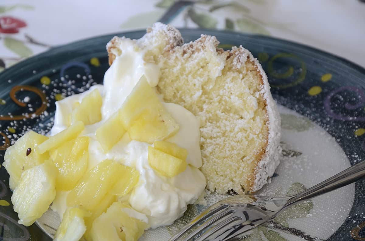 Coconut pound cake slice garnished with whipped cream and fresh pineapple chunks.
