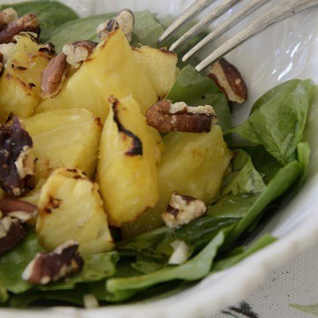 Baby spinach tossed with grilled pineapple, toasted pecans and Feta cheese in a salad bowl.