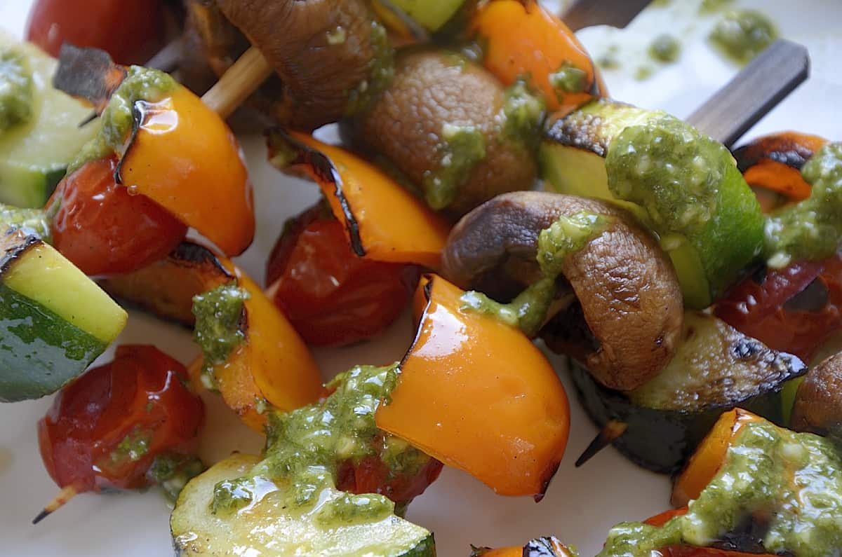 Skewers of raw pieces of zucchini, mushroom caps, cherry tomatoes and sweet pepper with chimichurri sauce.