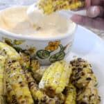 Charred, seasoned corn ribs dripping with garlic butter on a platter with Sriracha Dipping Sauce.