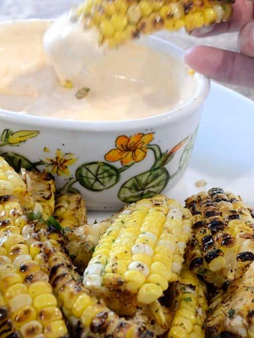 Charred, seasoned corn ribs dripping with garlic butter on a platter with Sriracha Dipping Sauce.