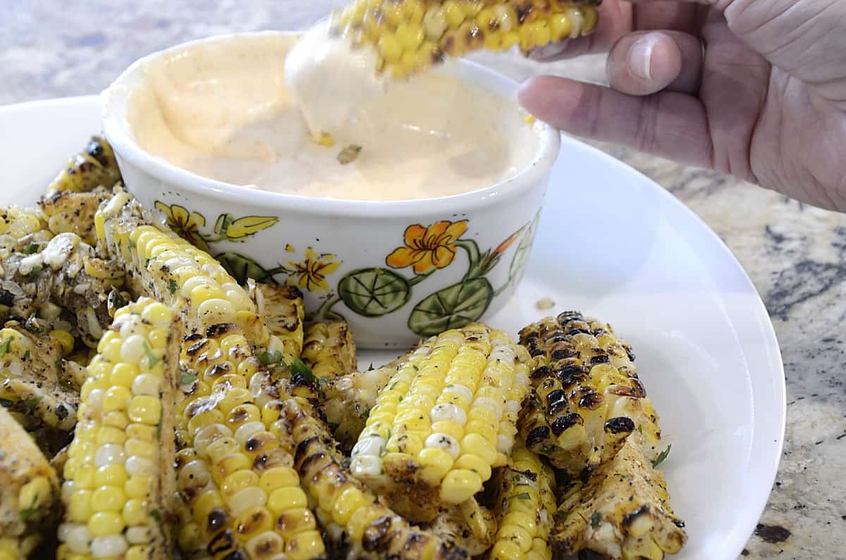 Charred, seasoned corn ribs dripping with garlic butter on a platter with Sriracha Dipping Sauce.