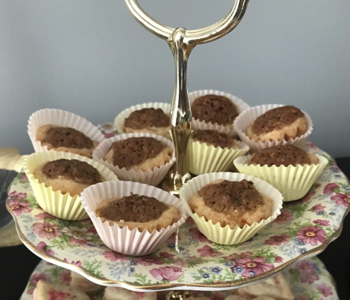 Pecan tassies in a frilly paper cup on a tiered tea plate.