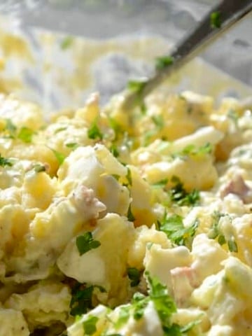 Close up of creamy potato salad with hard boiled eggs, celery, cucumber, sweet onion and parsley.