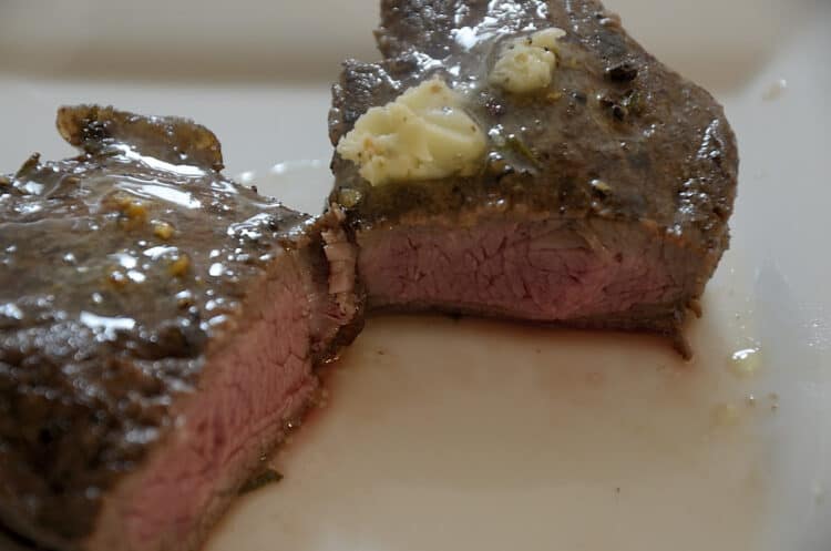 Close up of a medium rare, juicy, tender grilled sirloin steak topped with herb butter.