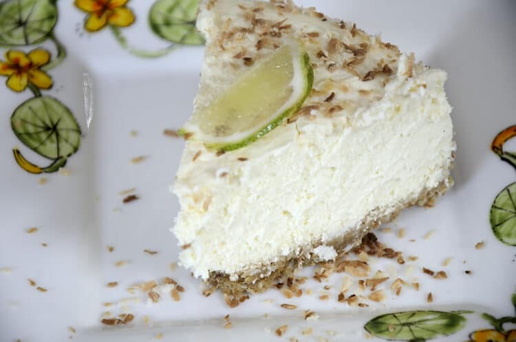 Piece of coconut lime cheesecake on a plate with lime and toasted coconut garnish.