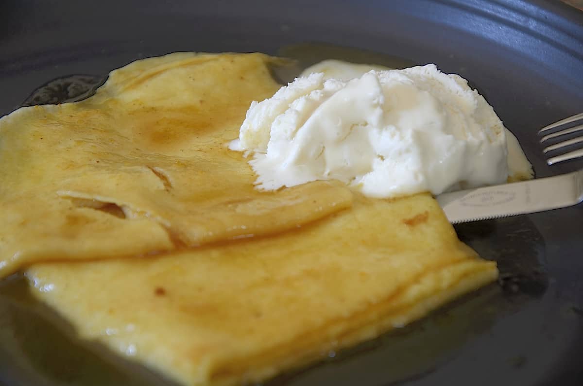 Folded crepes on a plate with Crepe Suzette sauce and a dollop of vanilla ice cream.