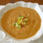 Close up of a bowl of chilled gazpacho soup garnished with diced tomato and cucumber.