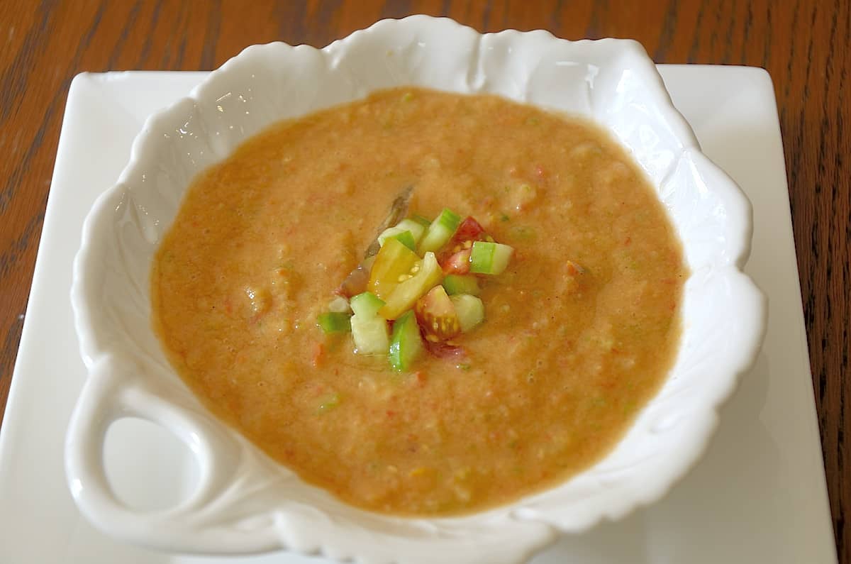 Close up of a bowl of chilled gazpacho soup garnished with diced tomato and cucumber.