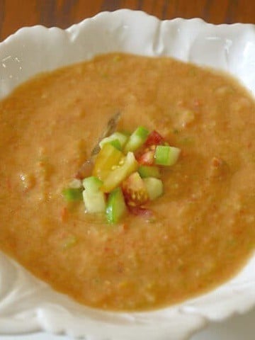 Close up of a bowl of chilled gazpacho soup garnished with diced tomato and cucumber.