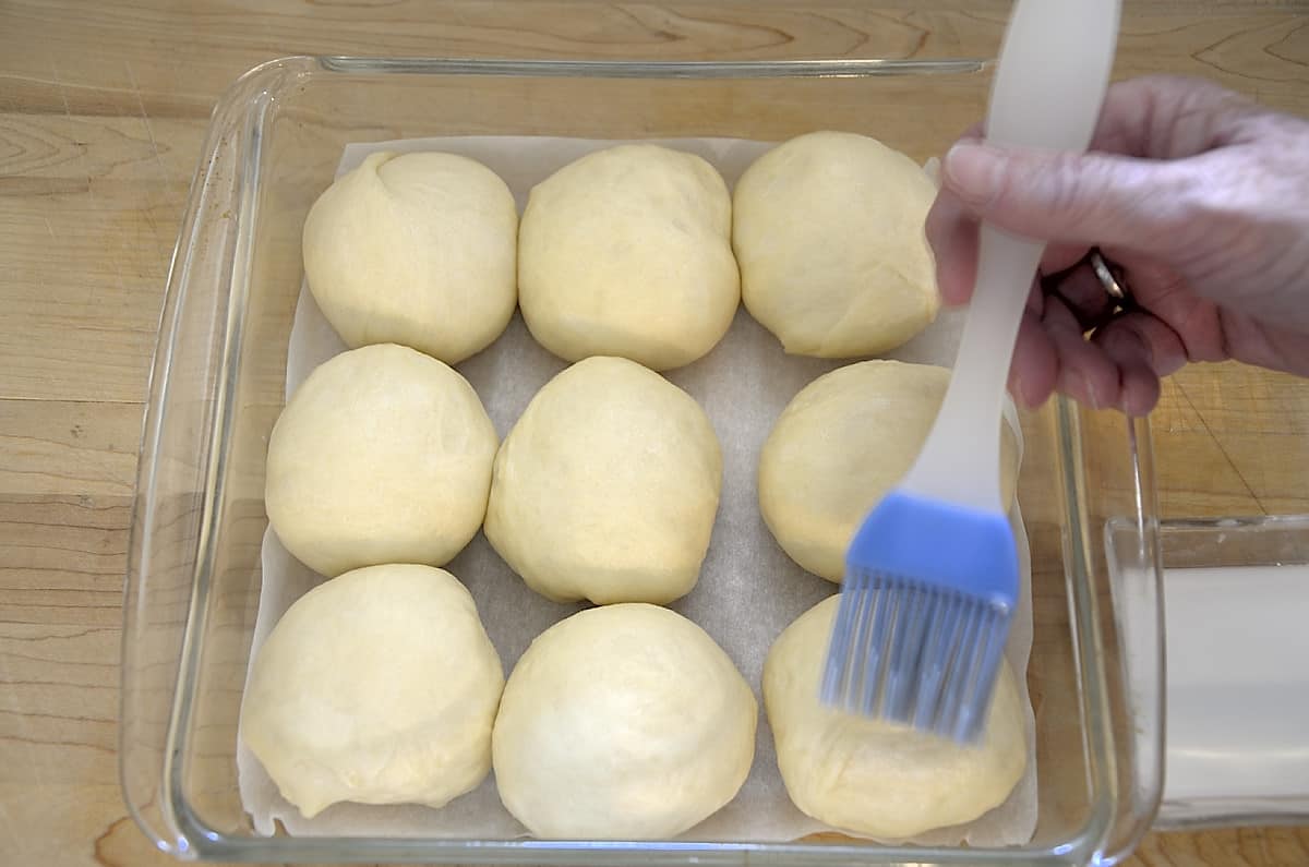 Brushing the top of the risen buns with milk before baking.